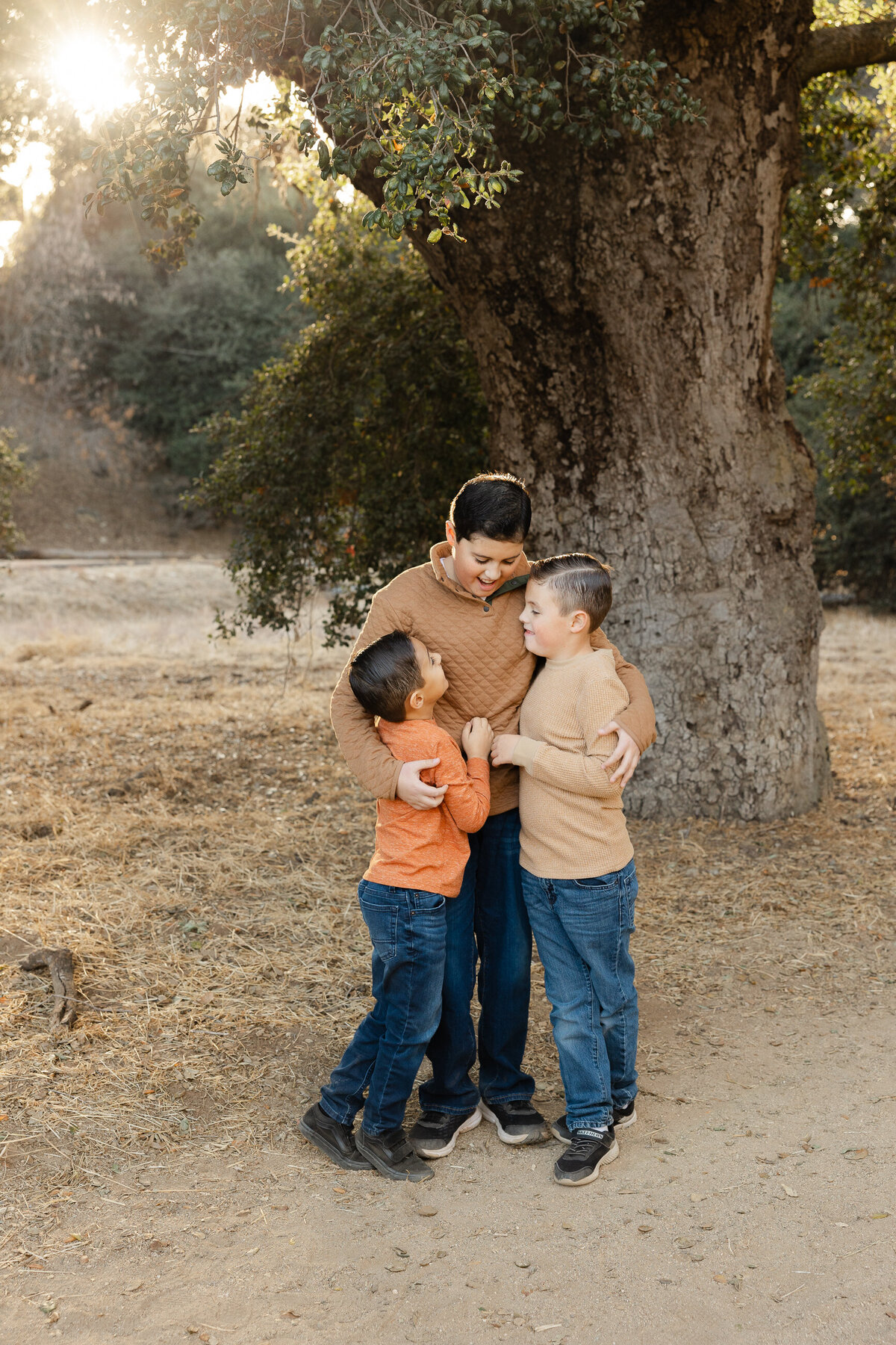 Three brothers hugging in front of large tree during fall family session. Photographed by Yucaipa family photographer Kaitlyn Dawn Photography.