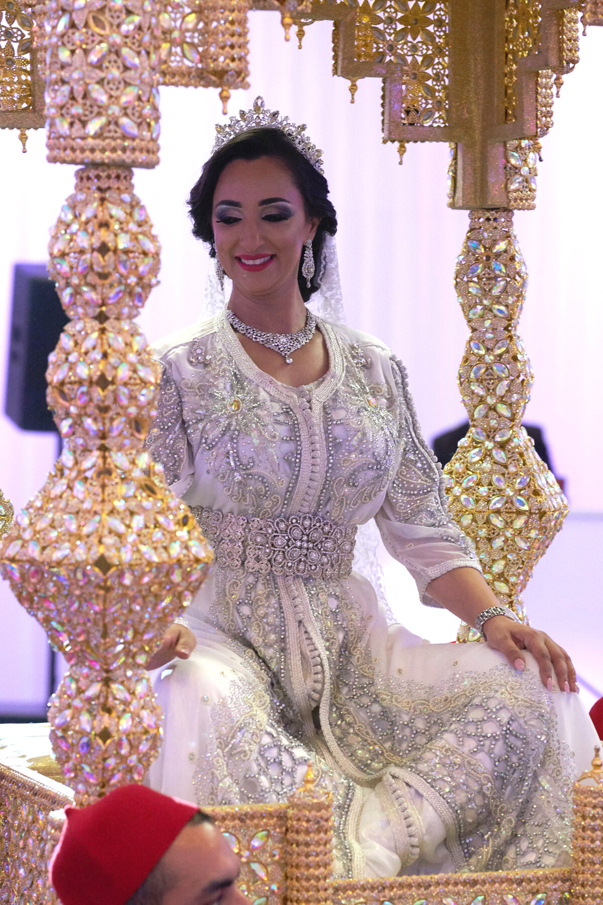 A bride sits cross-legged, showcasing her elegant bridal attire in a relaxed and natural pose. This image captures the bride’s grace and the detailed craftsmanship of her gown, highlighting the beauty and comfort of her wedding day look in a candid and charming moment.