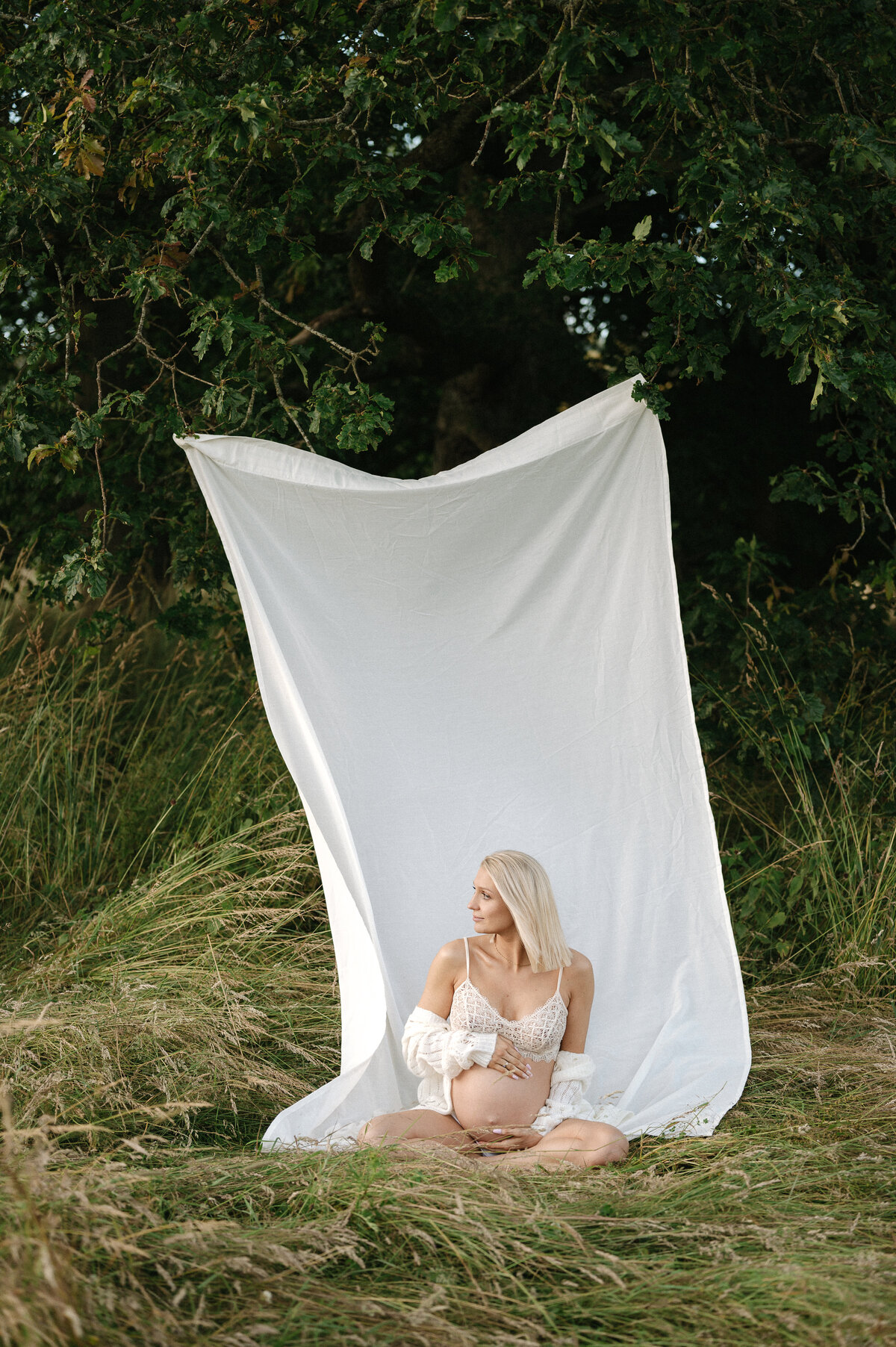Outdoor pegnancy photography of a woman in a field in front of a white sheet