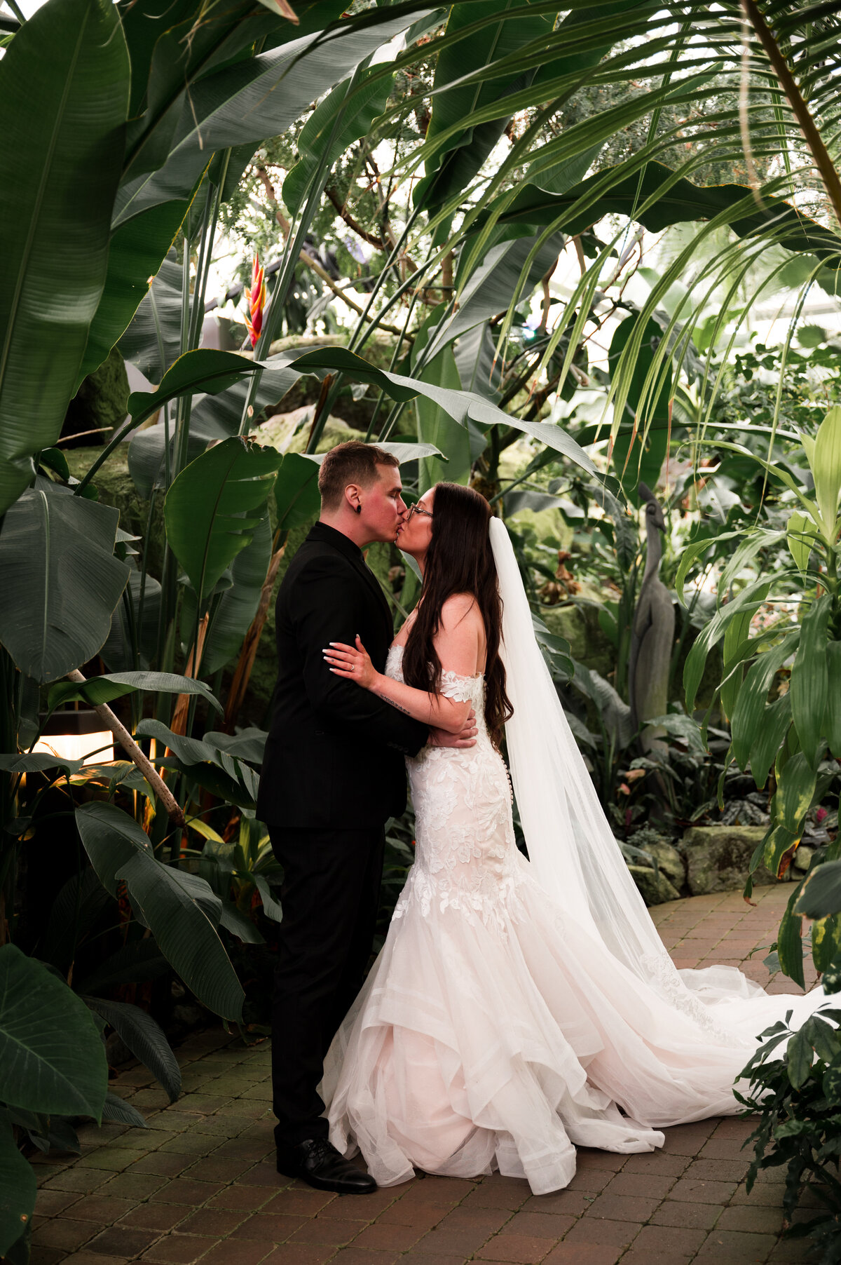 bride and groom surrounded by tropical plants kissing