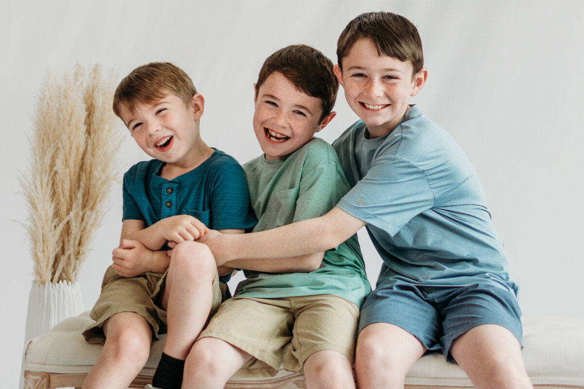 two older brothers tickling the youngest brother during a studio photoshoot in Bartlett, IL