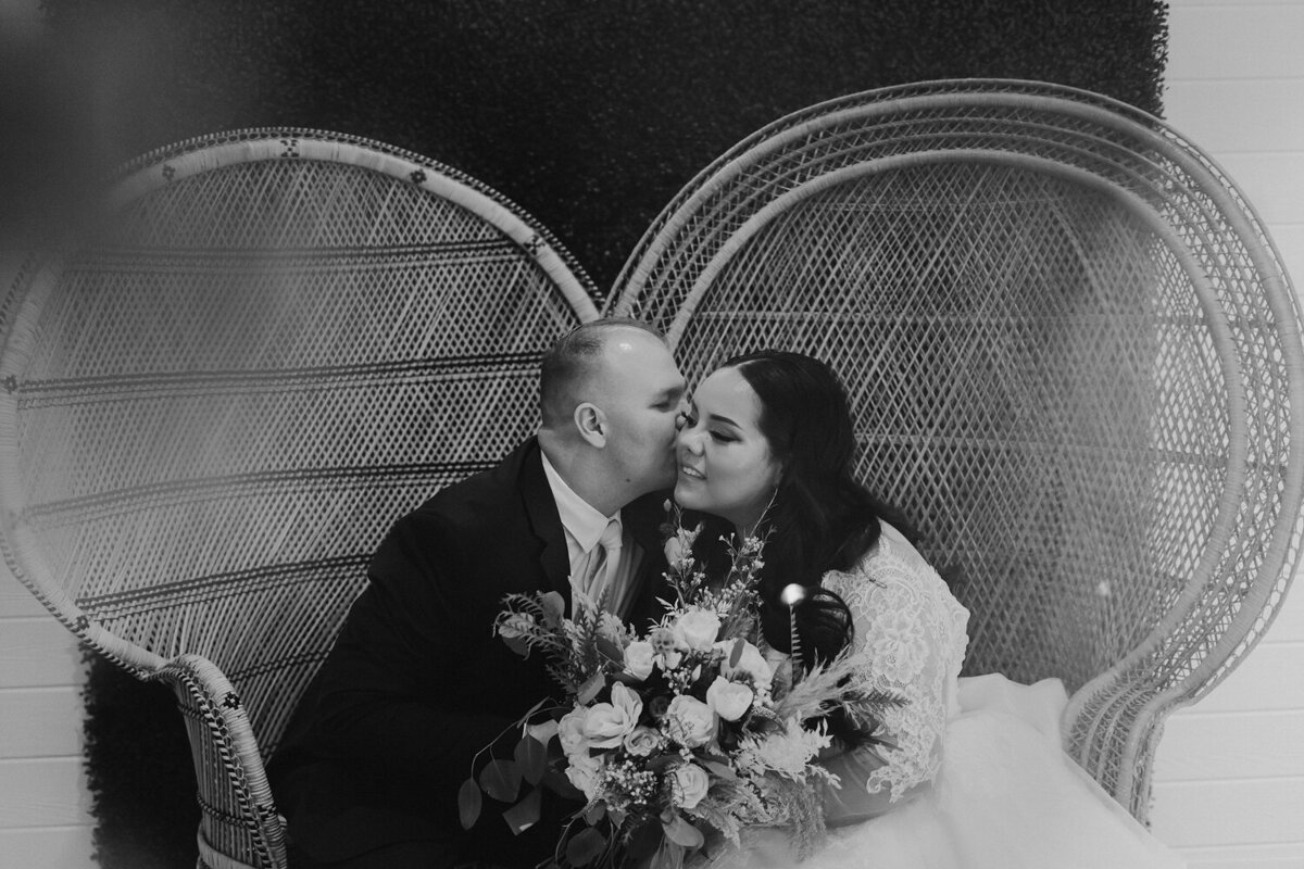 bride-and-groom-kiss-wicker-lounge-chair-wedding-ashton-hill-farm-cedar-rapids-iowa-storyteller-collective-photo-co