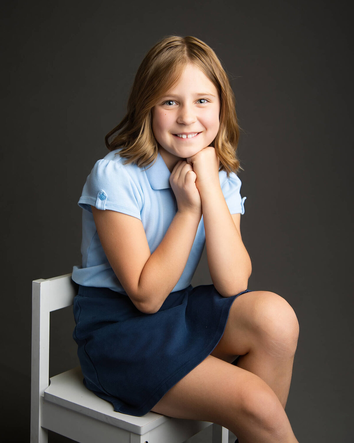 Girl in a school uniform posing on a chair with her chin on her hands during her las vegas school portrait session