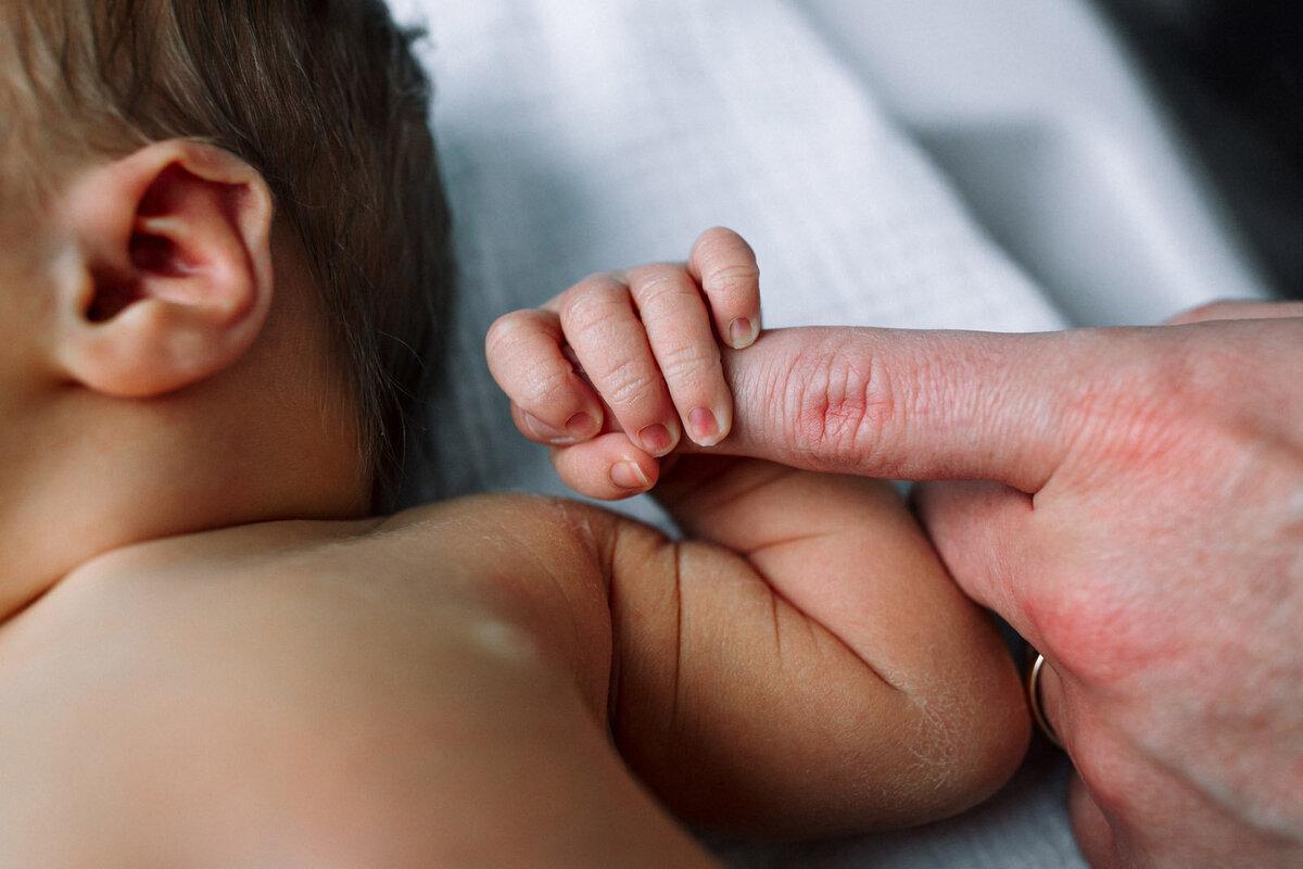 newborn hand wrapped around dad's finger with newborn laying in hospital bassinet