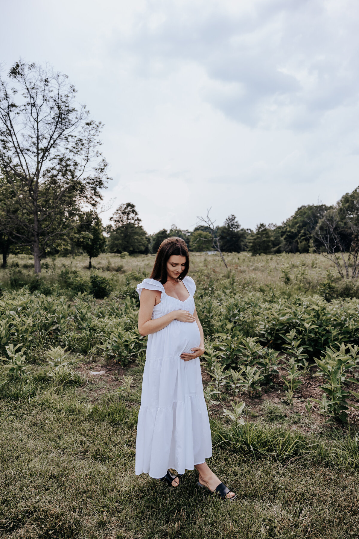 Nashville newborn photographer captures woman wearing white dress during outdoor maternity photos