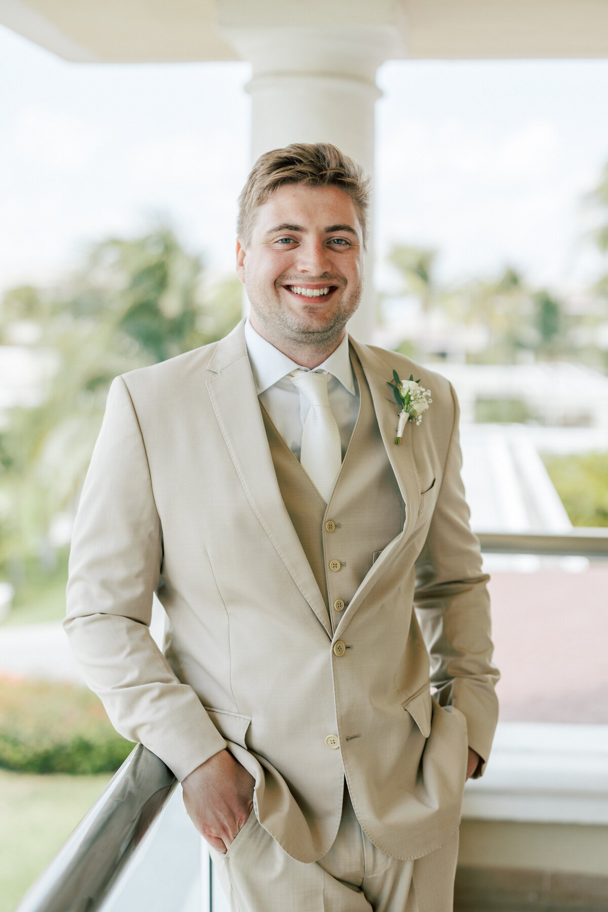 Groom on balcony in tan suit smiling ahead of Cancun ceremony, photographed by Philly-based wedding photographer.