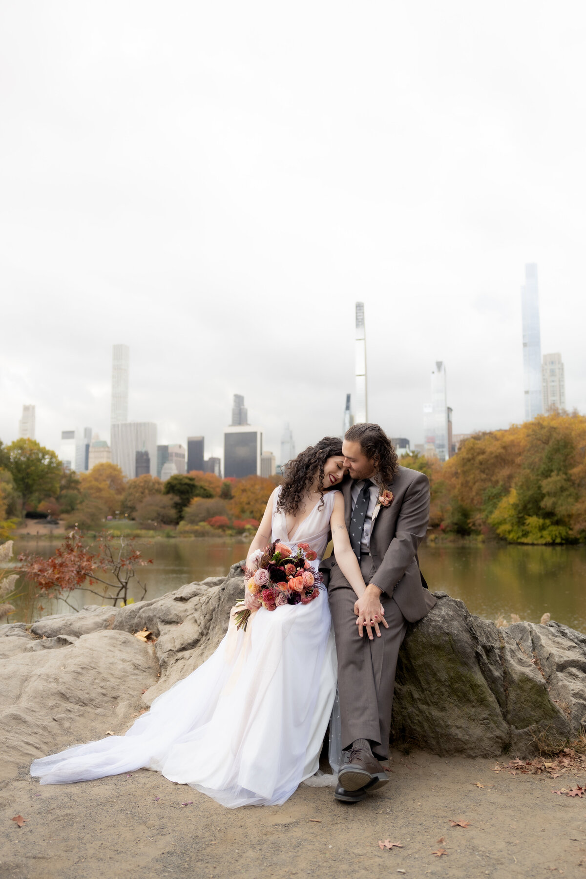 The couple standing close together surrounded by Central Park’s glowing fall foliage.