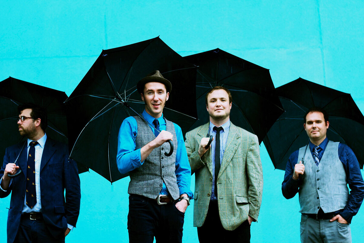 Band portrait Gordie and His Rhythm Boys all four members standing against blue backdrop holding open black umbrellas
