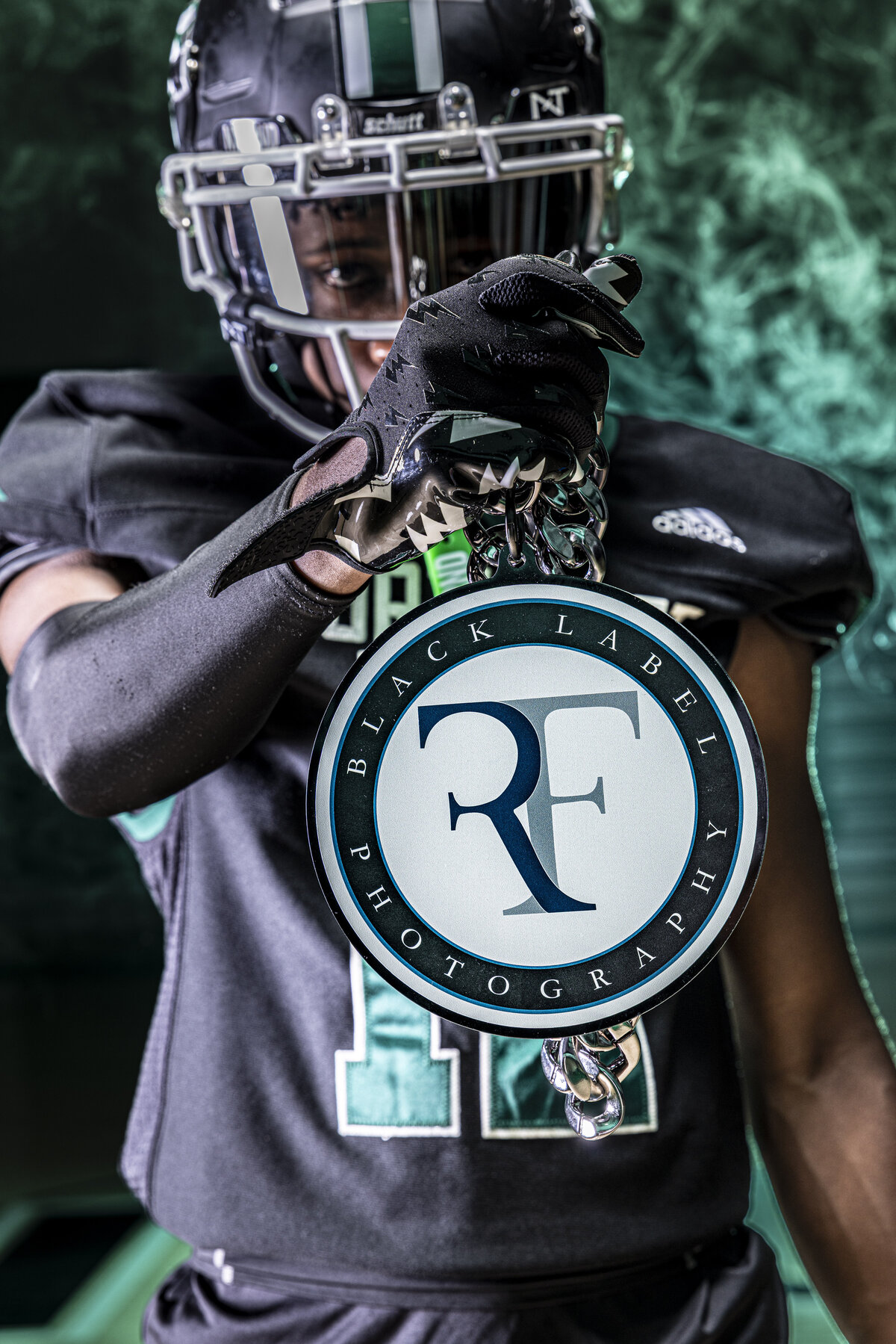 CT Photographer | Rob Faber Photography | Football Media Day- Football player in uniform holding RF sign promoting Rob Faber photography with green smoke in background.