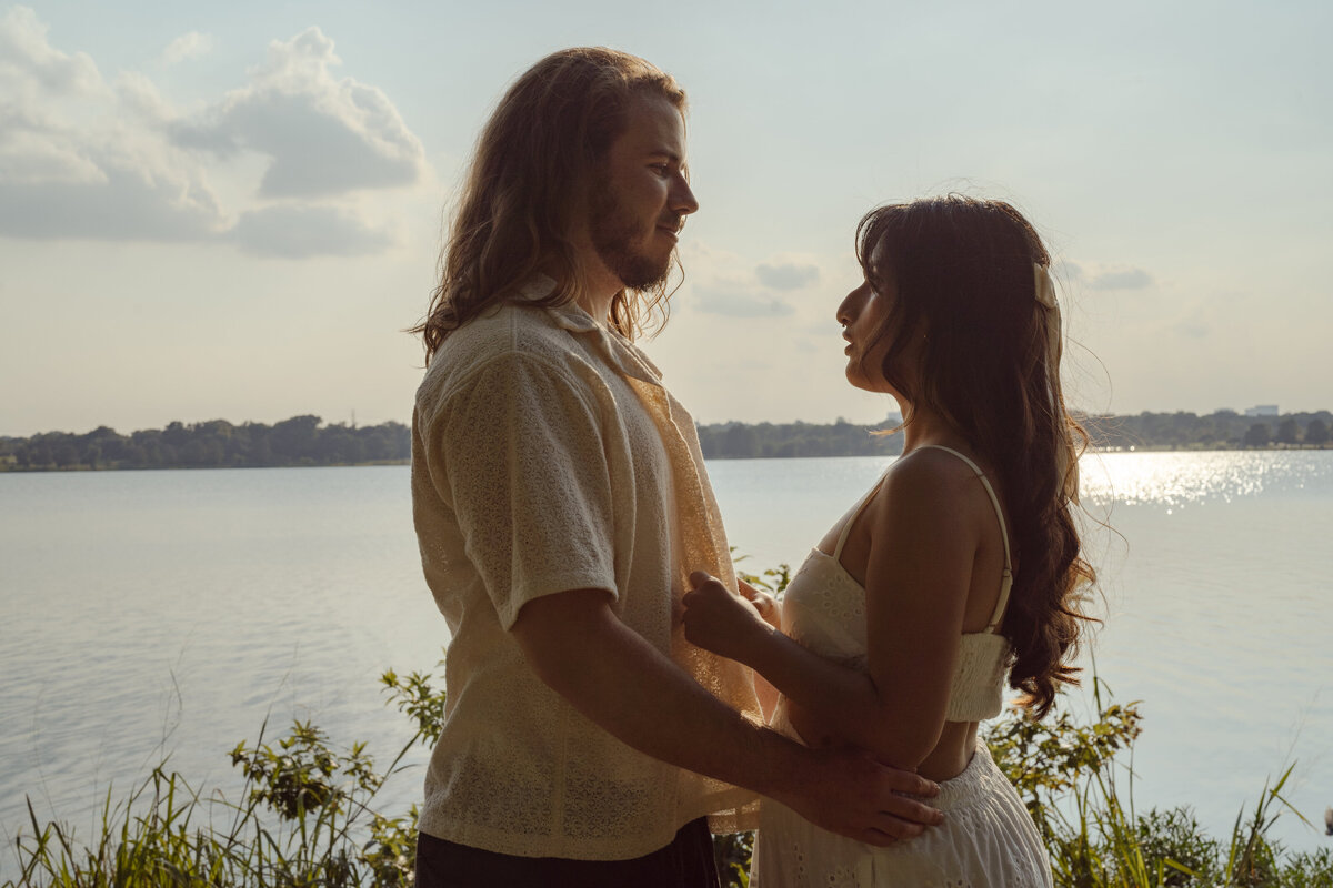 A scenic shot of a couple holding each other by the water at White Rock Lake, capturing a tender engagement moment.