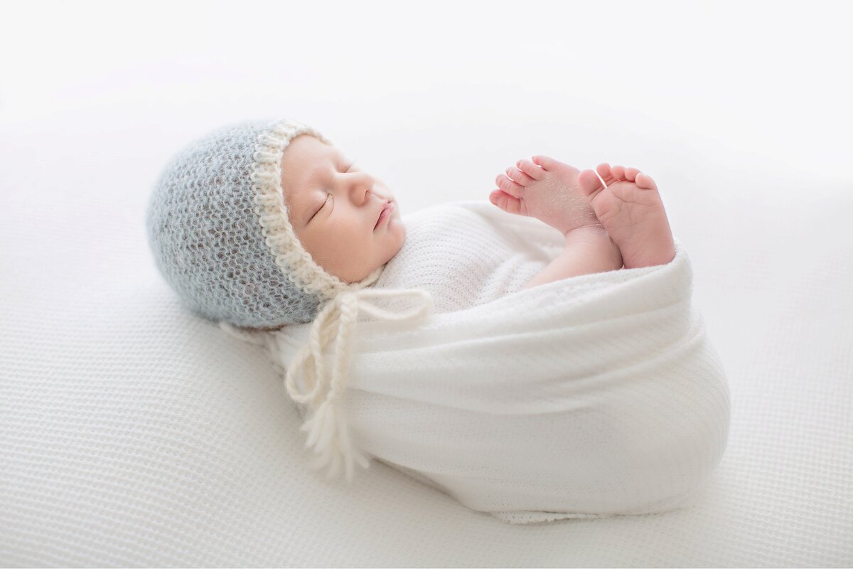 newborn baby swaddled with feet out wearing blue hat