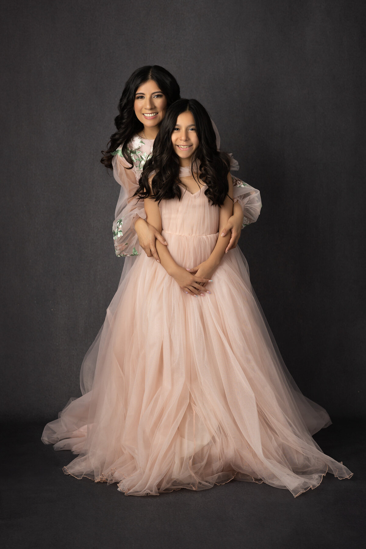 A Dallas family photographer captures the loving bond between a mother and daughter, both wearing matching soft pink dresses, smiling with joy.