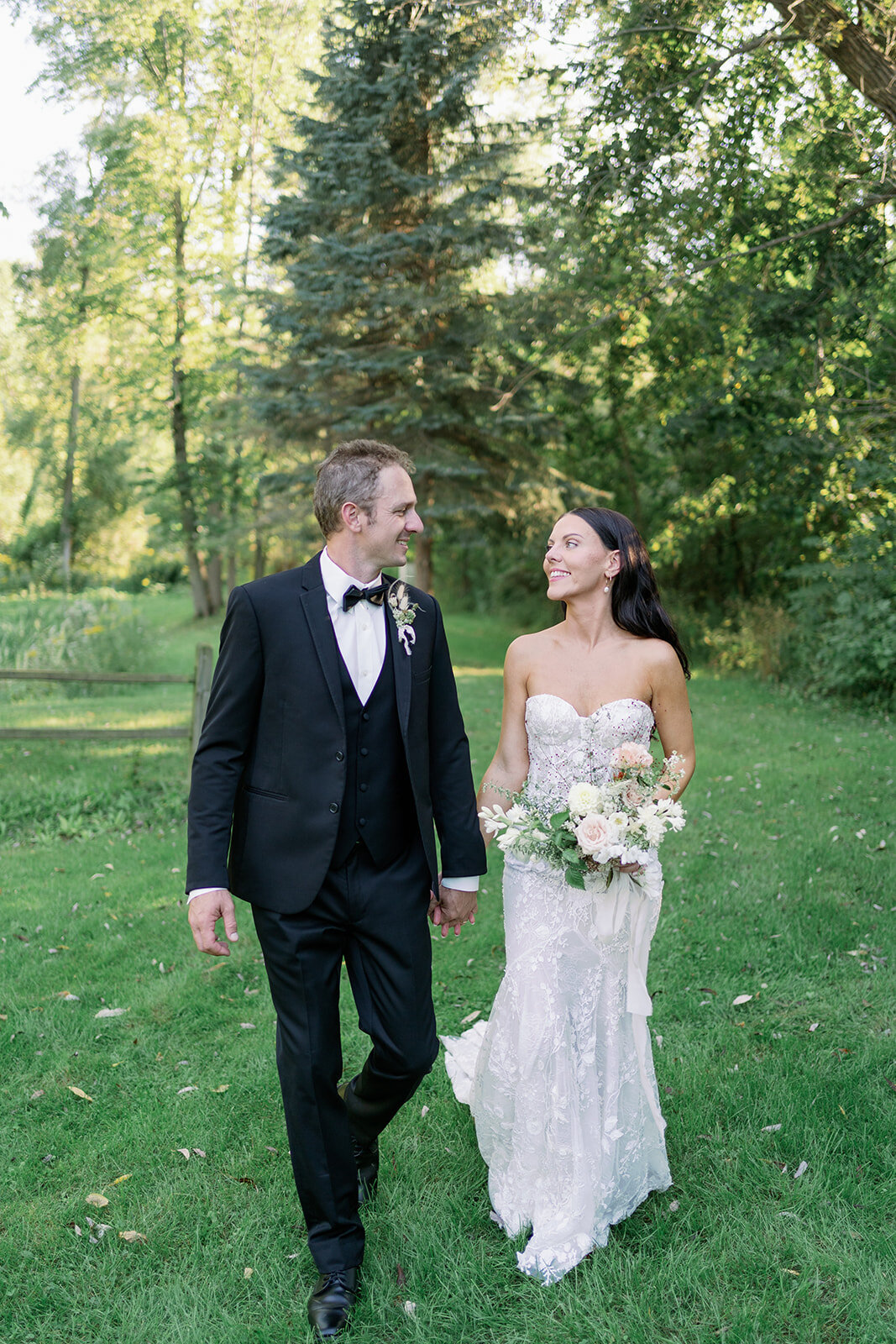 Newlyweds walking hand in hand across the lawn at Glasshouse Community during their intimate Michigan greenhouse wedding.
