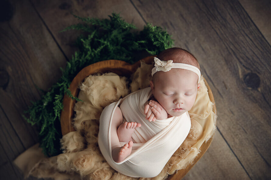 Baby with bow sleeps in a wooden heart bowl.