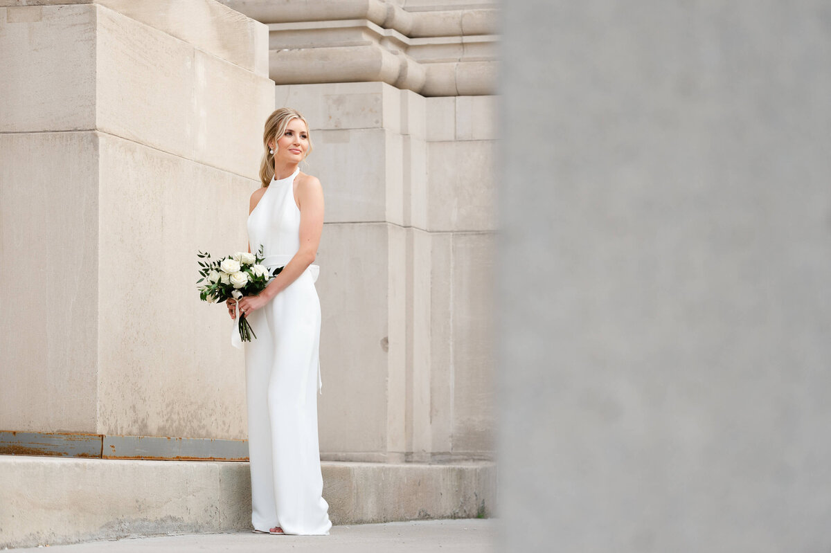 a full length portrait of a bride wearing a pantsuit and holding a bouquet taken outside the Chateau Laurier hotel by Ottawa wedding photographer JEMMAN Photography