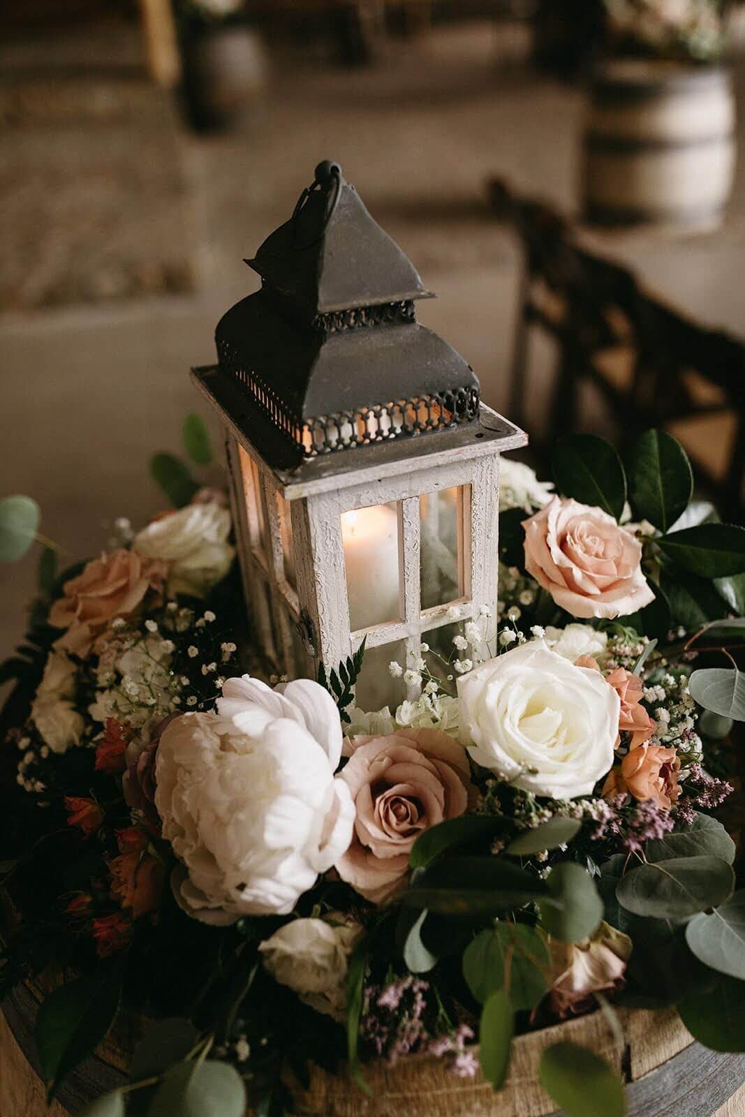 A flower arrangement by Flowers and Thyme sits atop a wine barrel with a candle lantern.