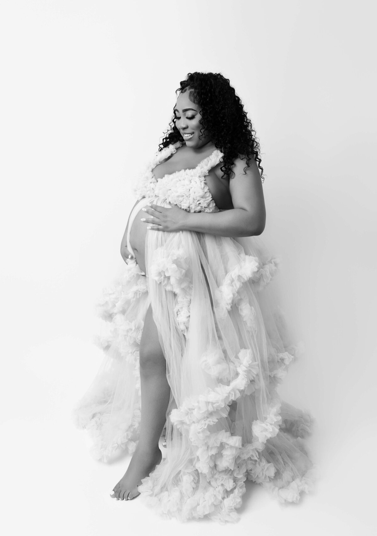 "Black and white image of a pregnant woman gently looking at her stomach during a NYC maternity photography session, capturing the serene and intimate moment of anticipation