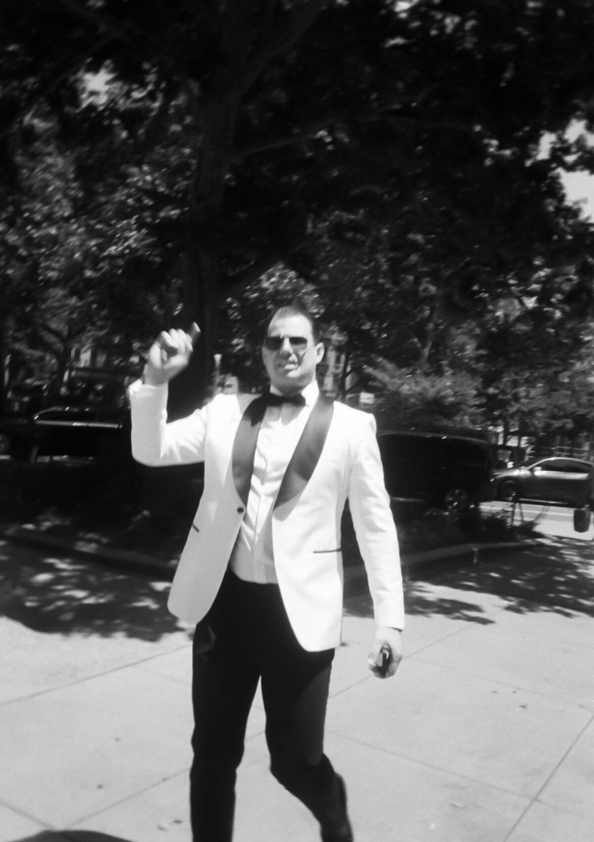 Black and white film photo of the groom in a white tuxedo jacket walking outside in New York City during Japna and Chris’s Hotel Chelsea elopement, captured by NYC wedding photographer Perry Hancock.