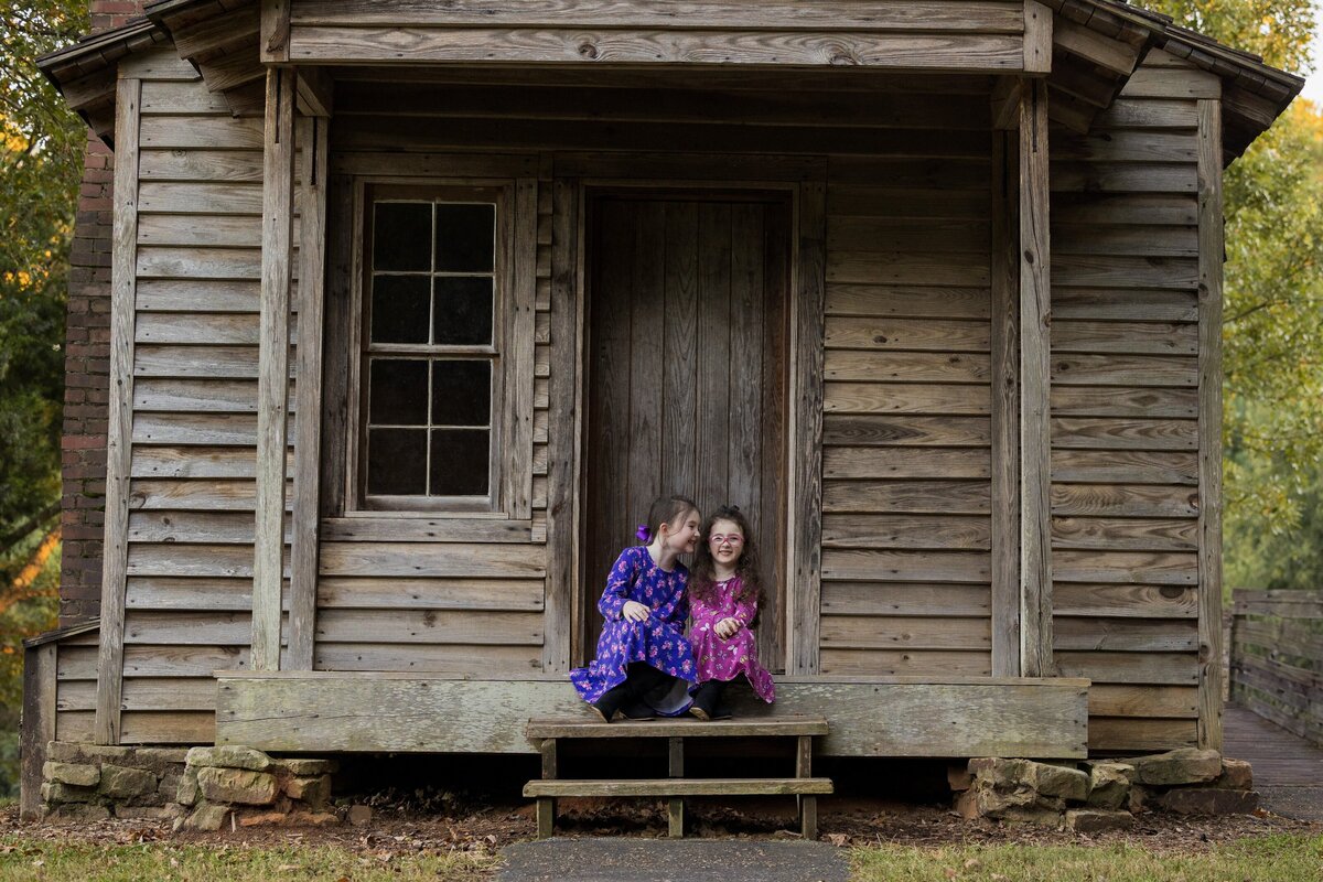 two children sitting on a porch of a log cabin