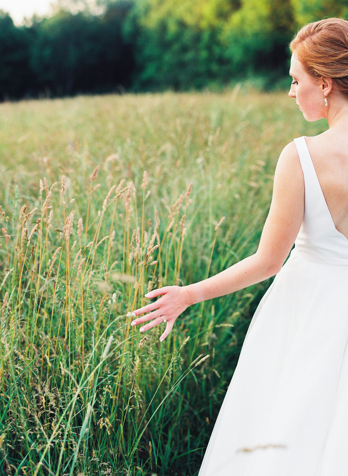 Bride running her fingers through tall grass in a field