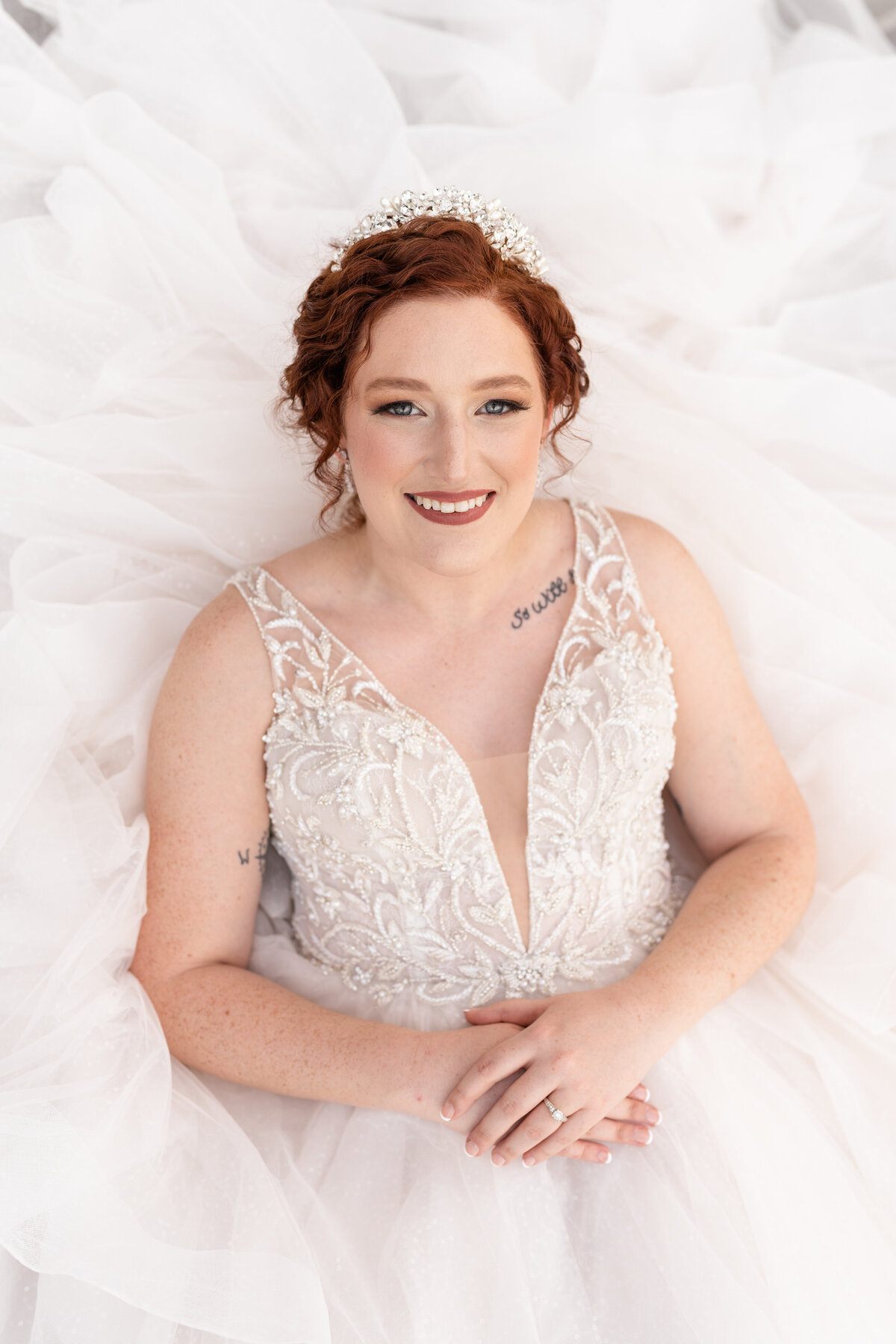 Bride laying down in bridal gown and tiara while smiling up at camera