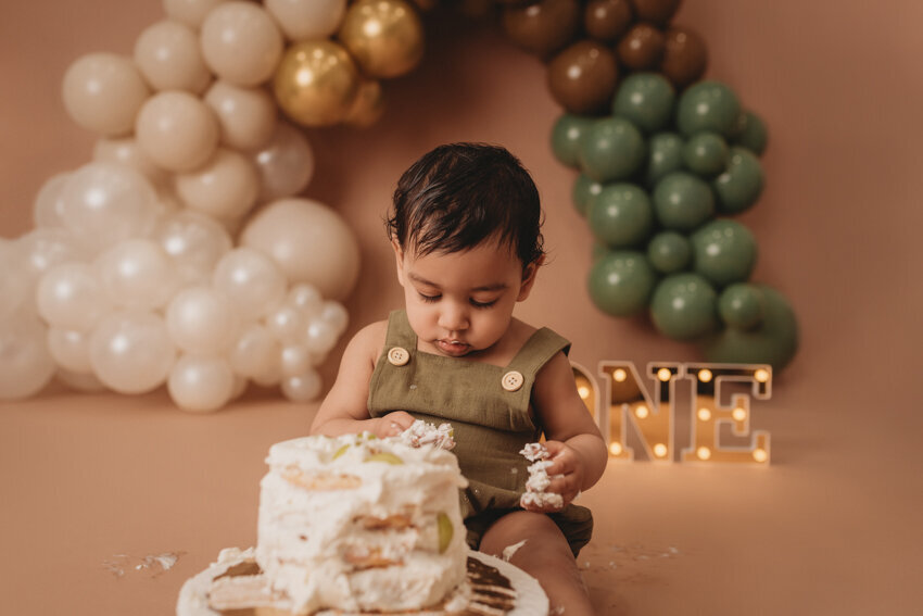 Cake smash milestone session with Atlanta, Georgia cake smash photographer. Milestone photography session with earthy tones, balloon garland and sweet baby boy eating cake for his first birthday.