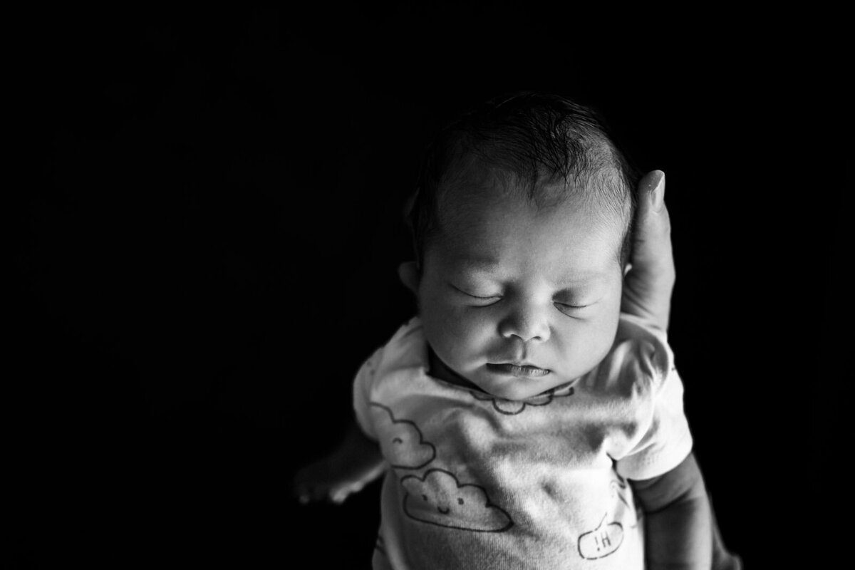 sleeping newborn wearing onesie with clouds held in mom's hand