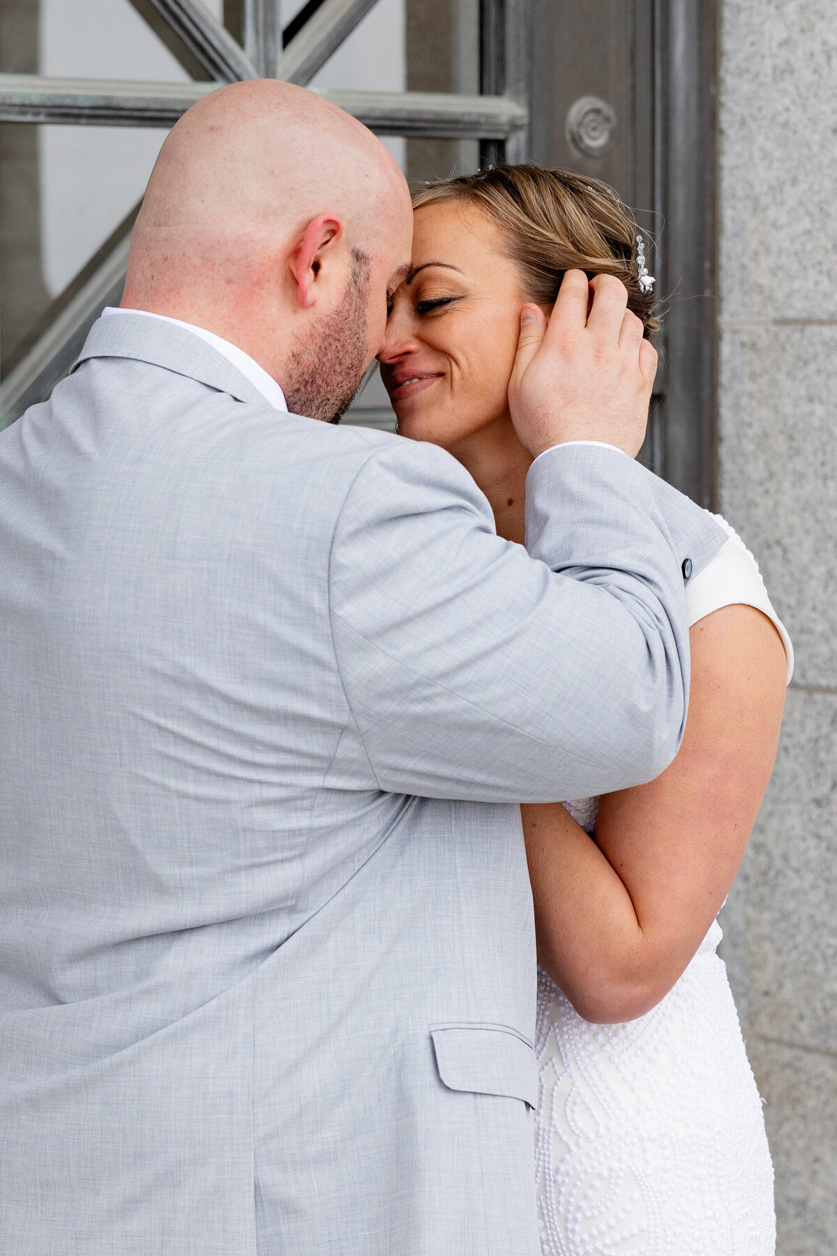 A groom holds his bride’s face tenderly, their foreheads touching as they share an intimate moment.