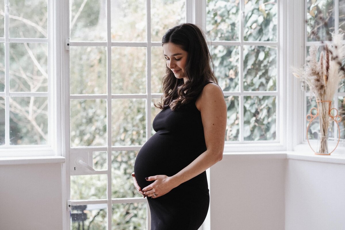Curly brown haired pregnant woman lovingly holds her baby bump
