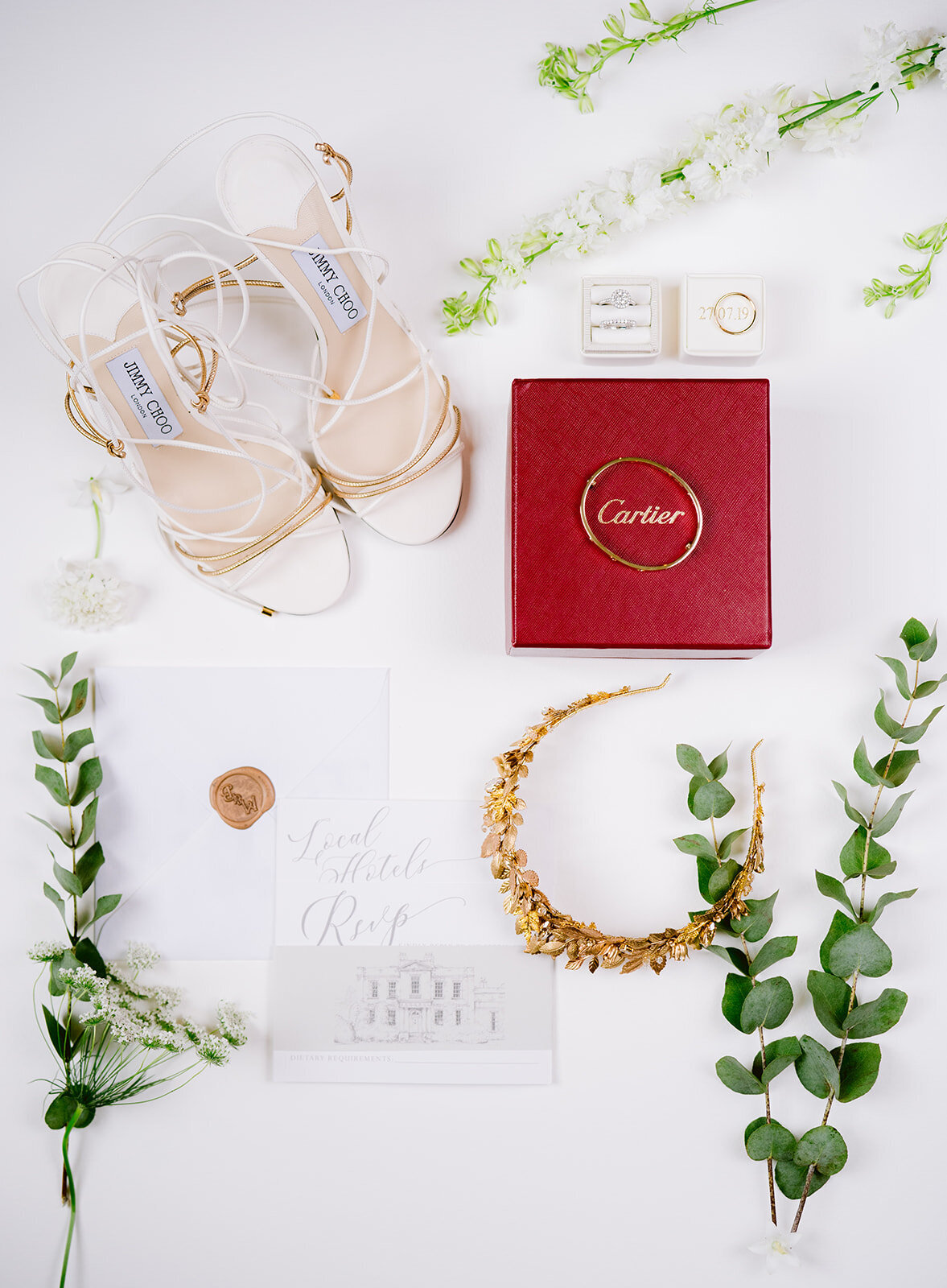 Flat lay photograph of the brides wedding details including a crown I wouldn't invitation I can't see a bracelet and Jimmy Choo wedding shoes and rings