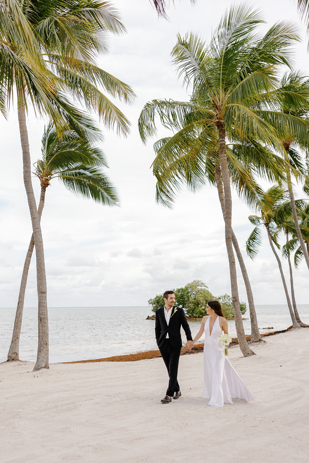 A dreamy, tropical setting as the couple walks along the beachfront after their vows. Florida Keys micro wedding captured by Claudia Amalia Wedding Photography.