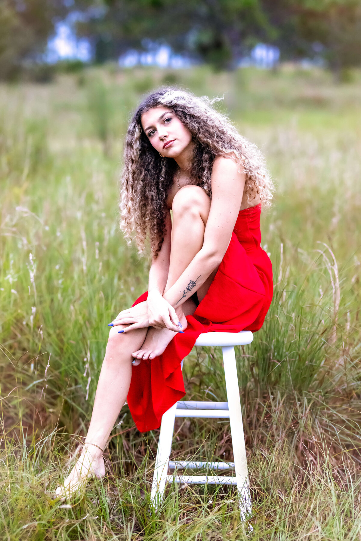 Senior girl leaning against a stool while wearing a vibrant red dress in Winter Garden.