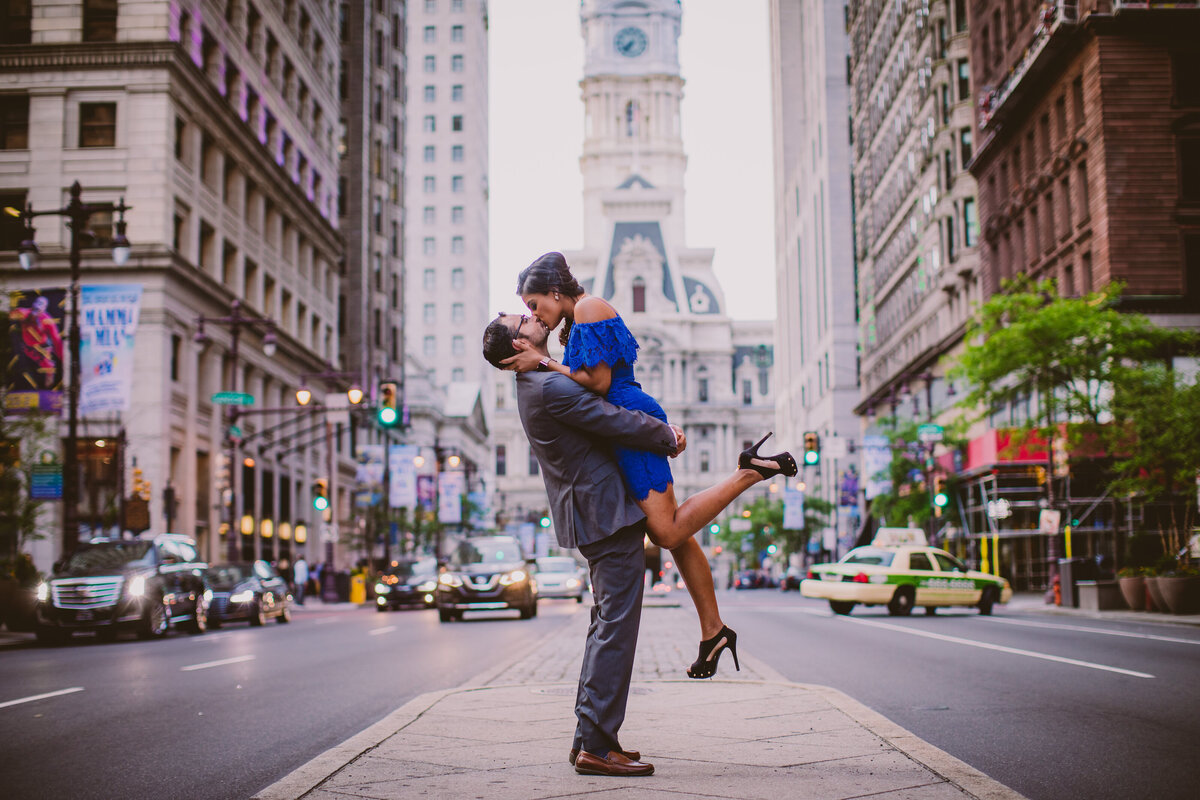 An engaged couple kiss while picked up in the air on broad street near the philadelphia city hall