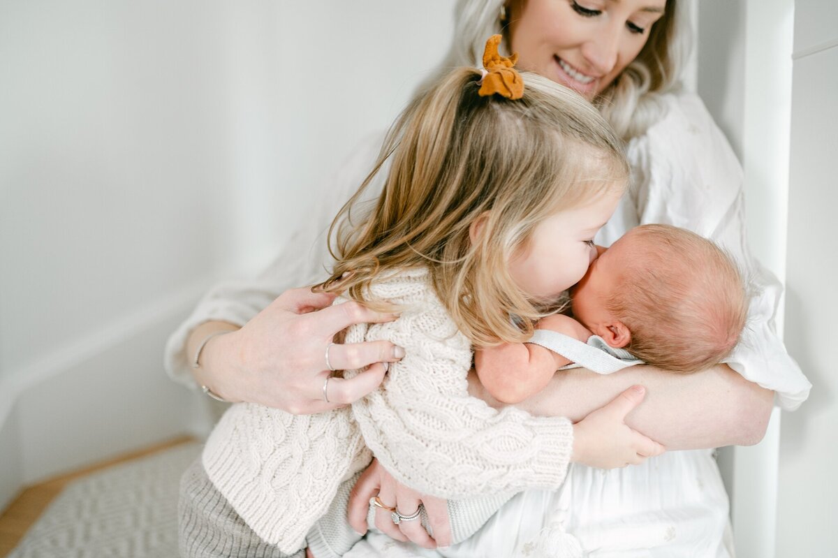 Older sister leans over to kiss her newborn brother during a Milwaukee newborn session