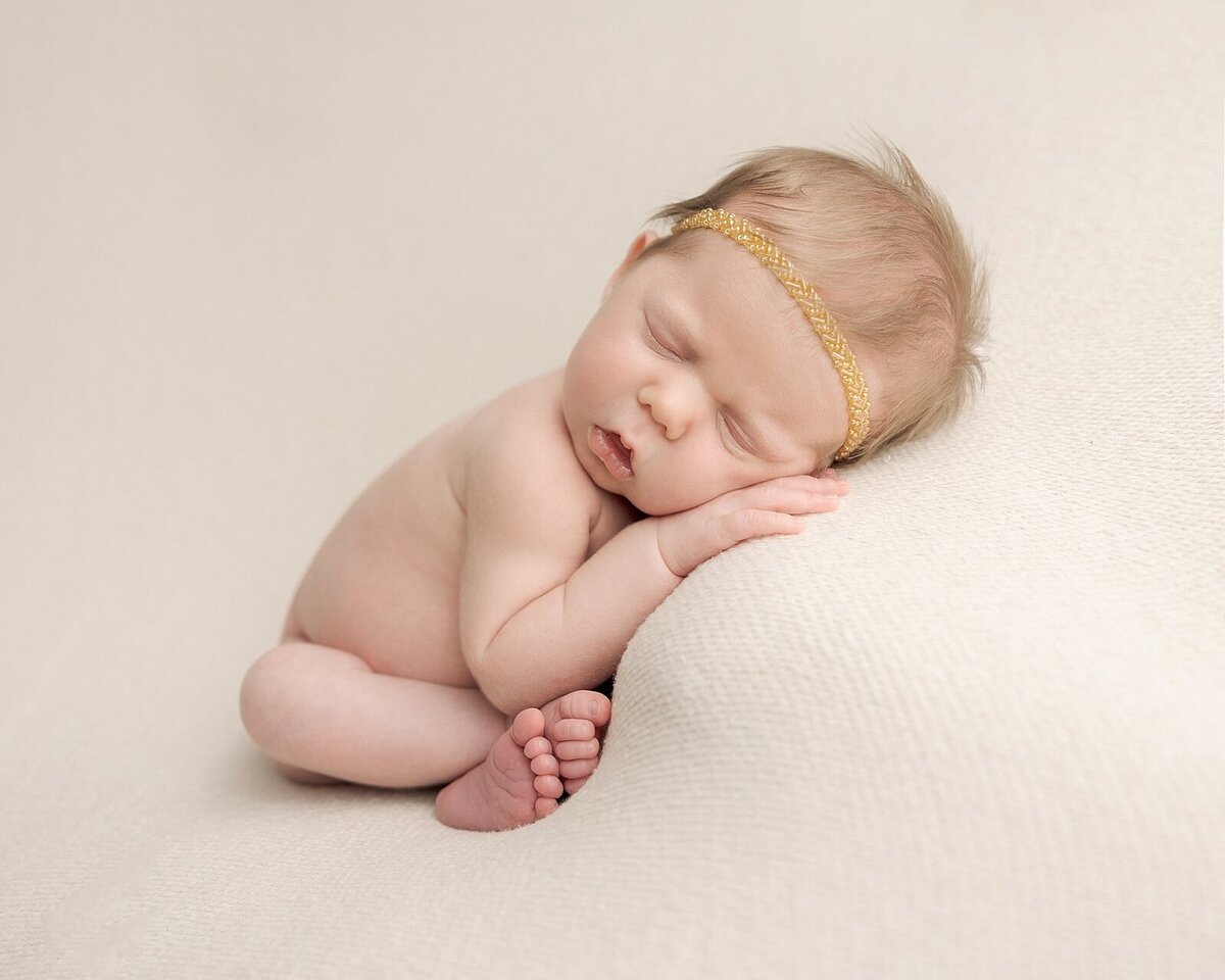 baby girl with gold headband on cream blanket