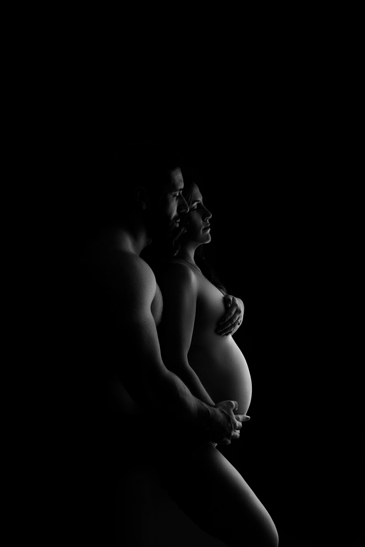 Maternity photos captured by top London, ON Maternity Photographer Amy Perrin-Ogg. Woman is facing side profile to the camera and her husband behind her touching her belly.
