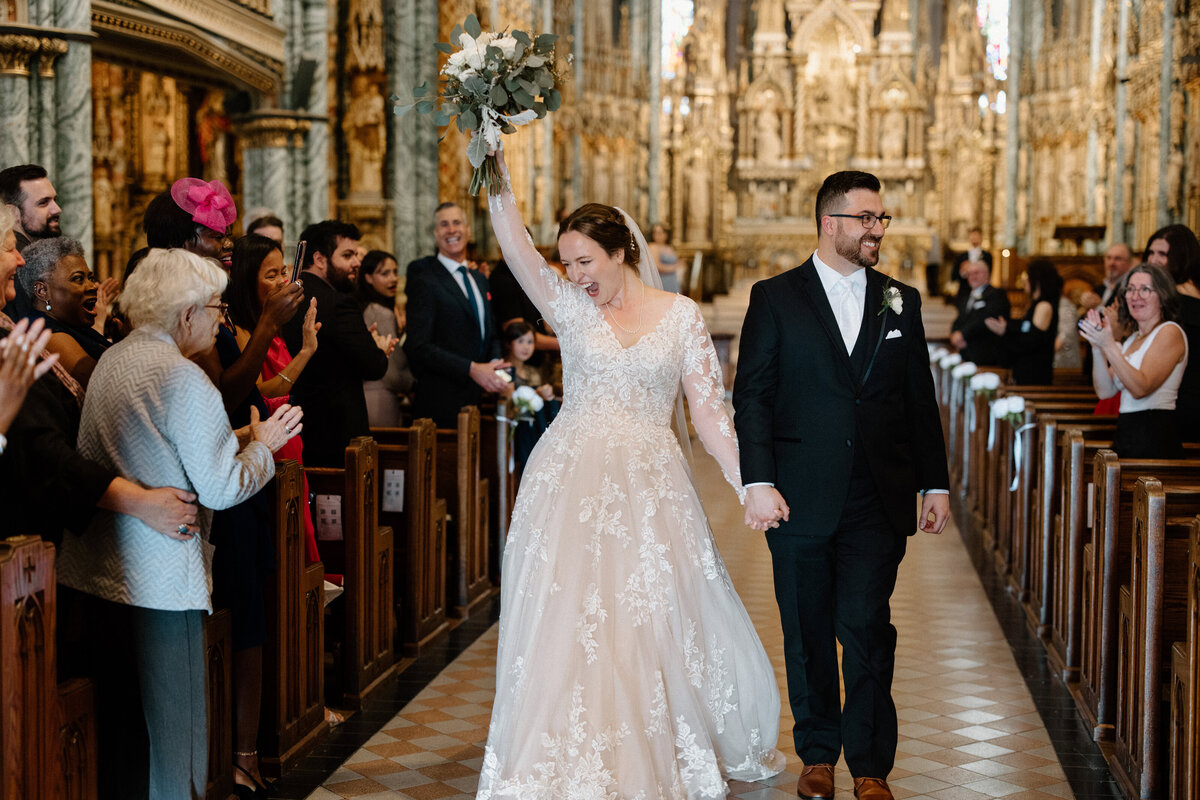 A bride looks victorious as she and the groom head outside of the church