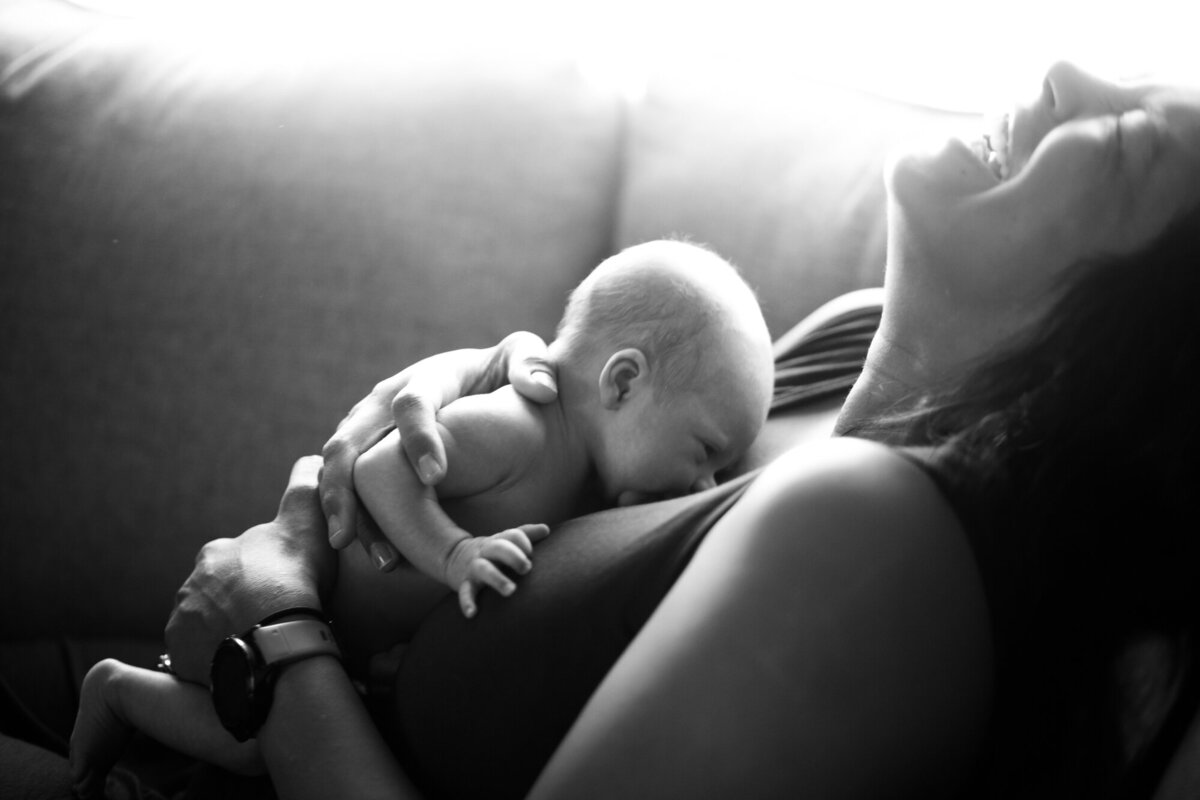 black and white image of a mom laughing with newborn baby lying on her chest