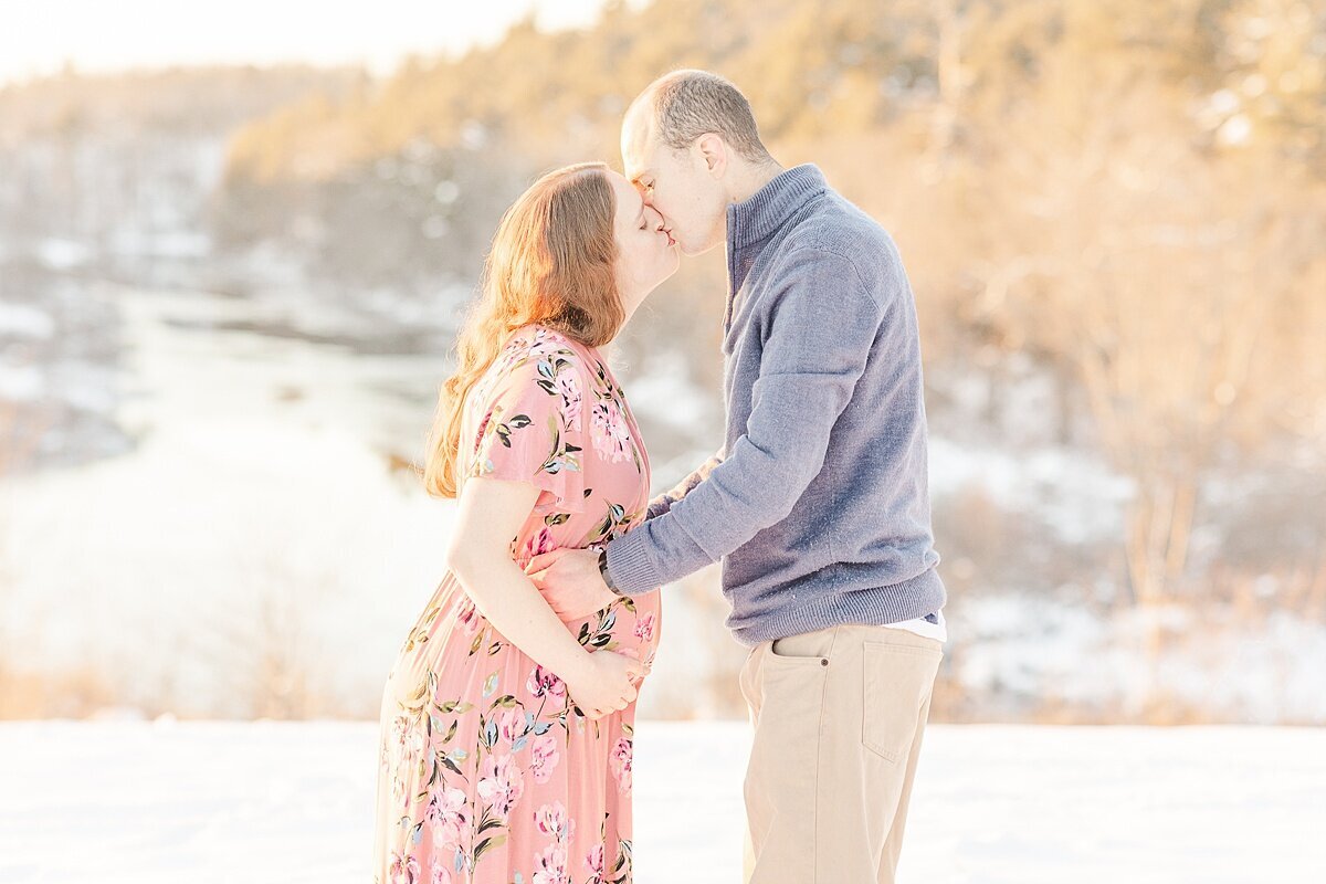 parents kiss during snowy winter maternity photo session with Sara Sniderman Photography in Medfield Massachusetts