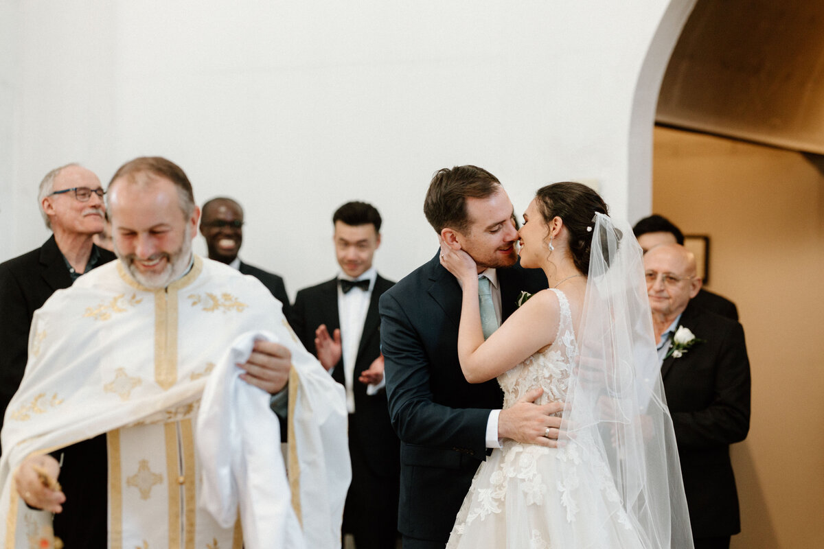 A couple kiss in front of the priest and guests after they get married