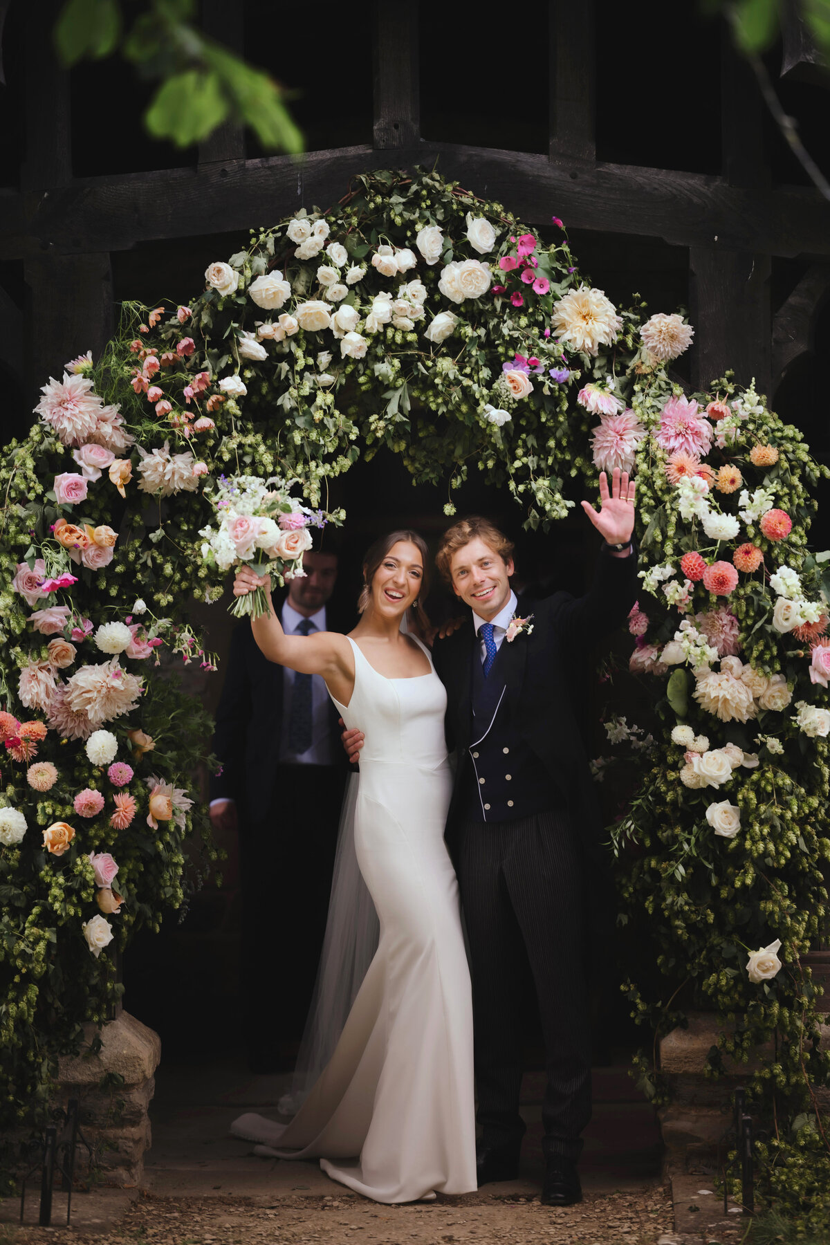Married couple outside floral archway in traditional Cotswold church