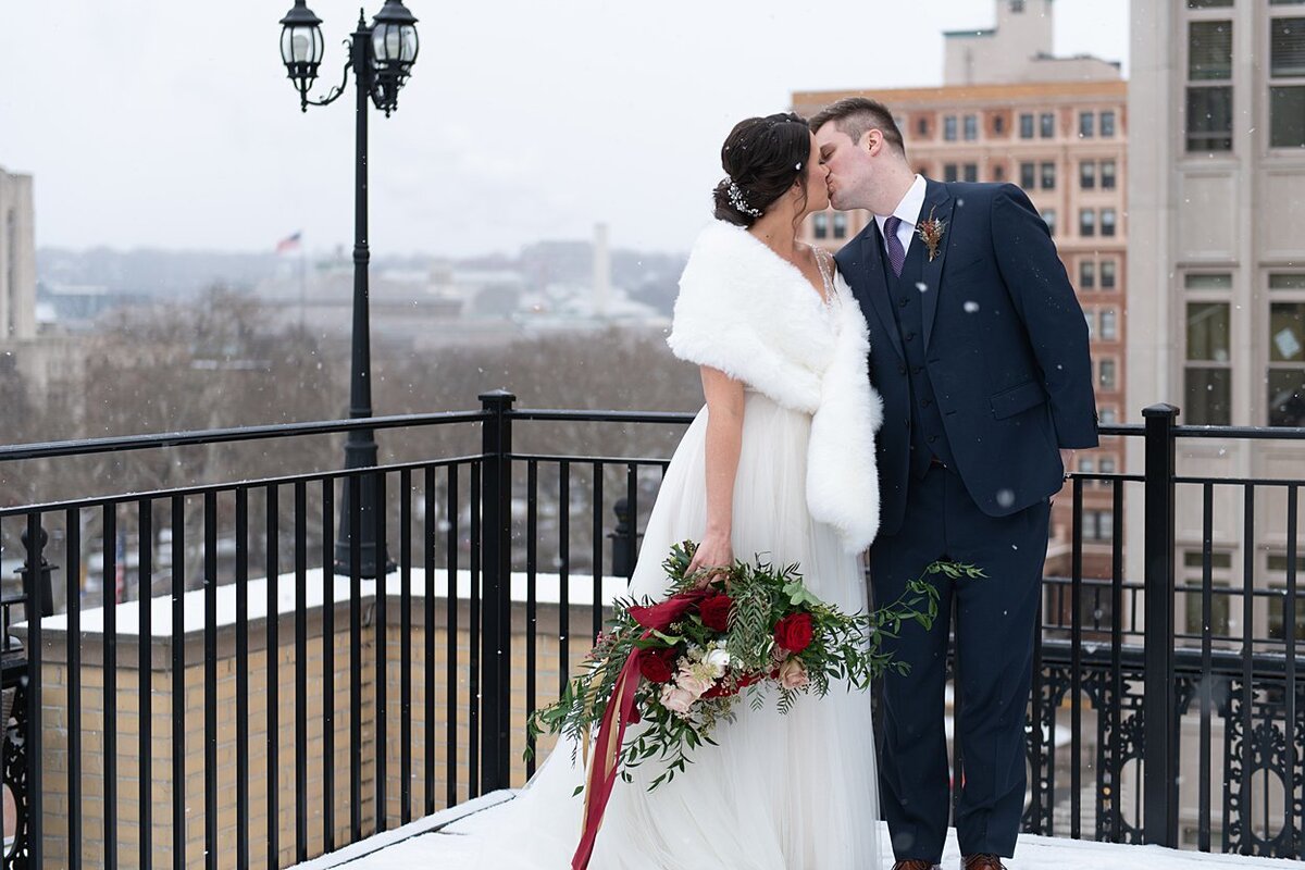 Groom kissing Bride in fur wrap on snowy rooftop at University Club in Pittsburgh, PA