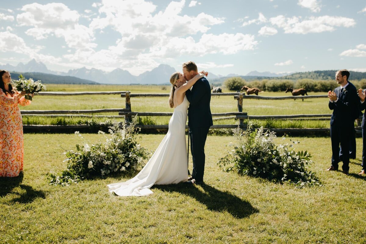 bride-and-groom-kiss-ceremony-ground-florals-Diamond-Cross-Ranch-wedding-July-green-white-11