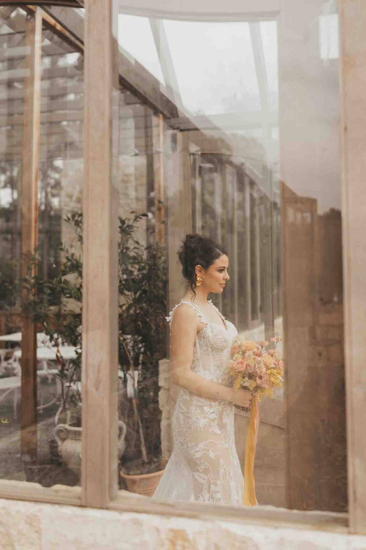 gorgeous bride holds her wedding bouquet while allyson blankenburg takes her photo through a window of a rose farm garden.