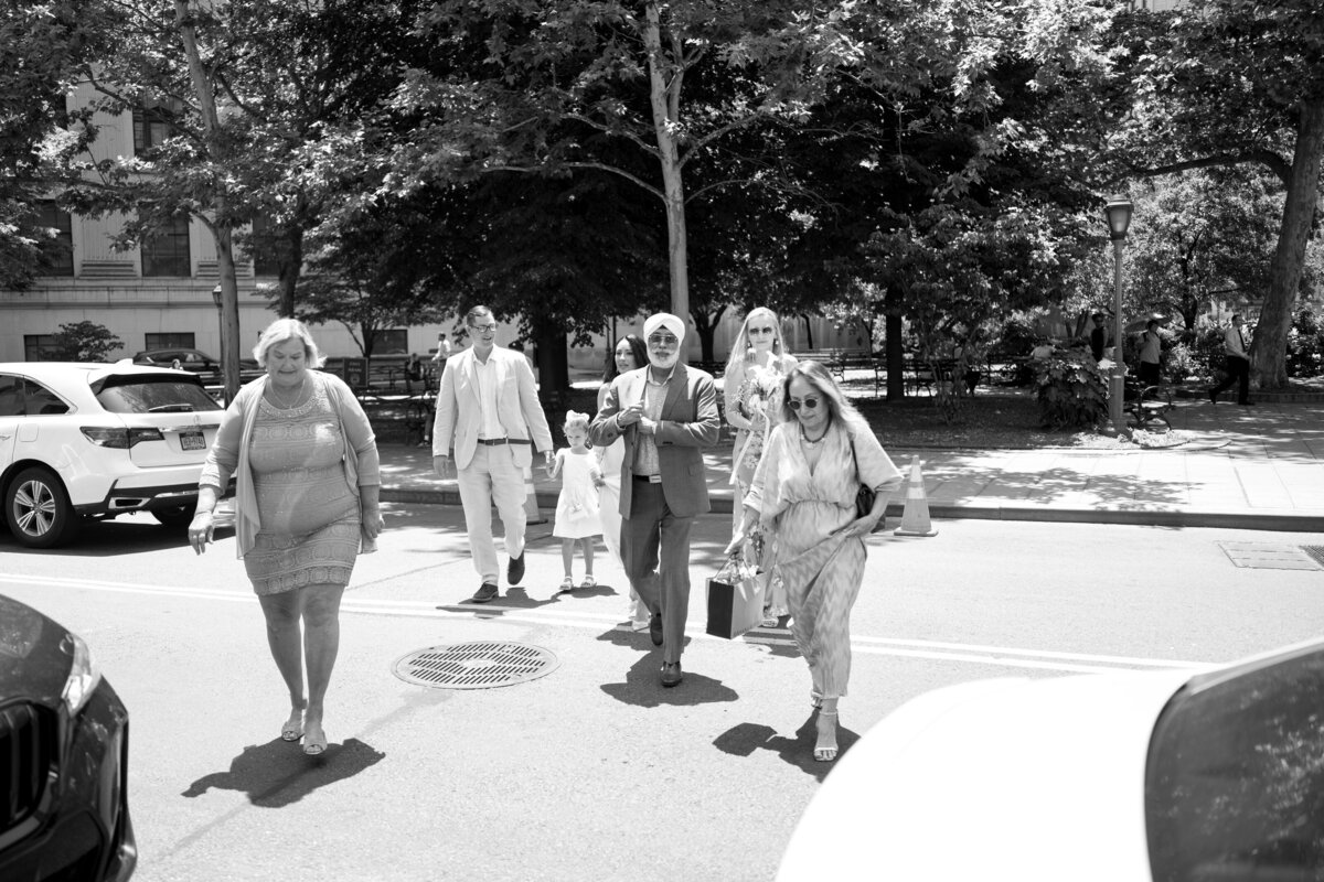 Black and white photo of family and guests walking together toward New York City Hall for Japna and Chris’s intimate elopement, captured in a candid documentary style by NYC wedding photographer Perry Hancock.