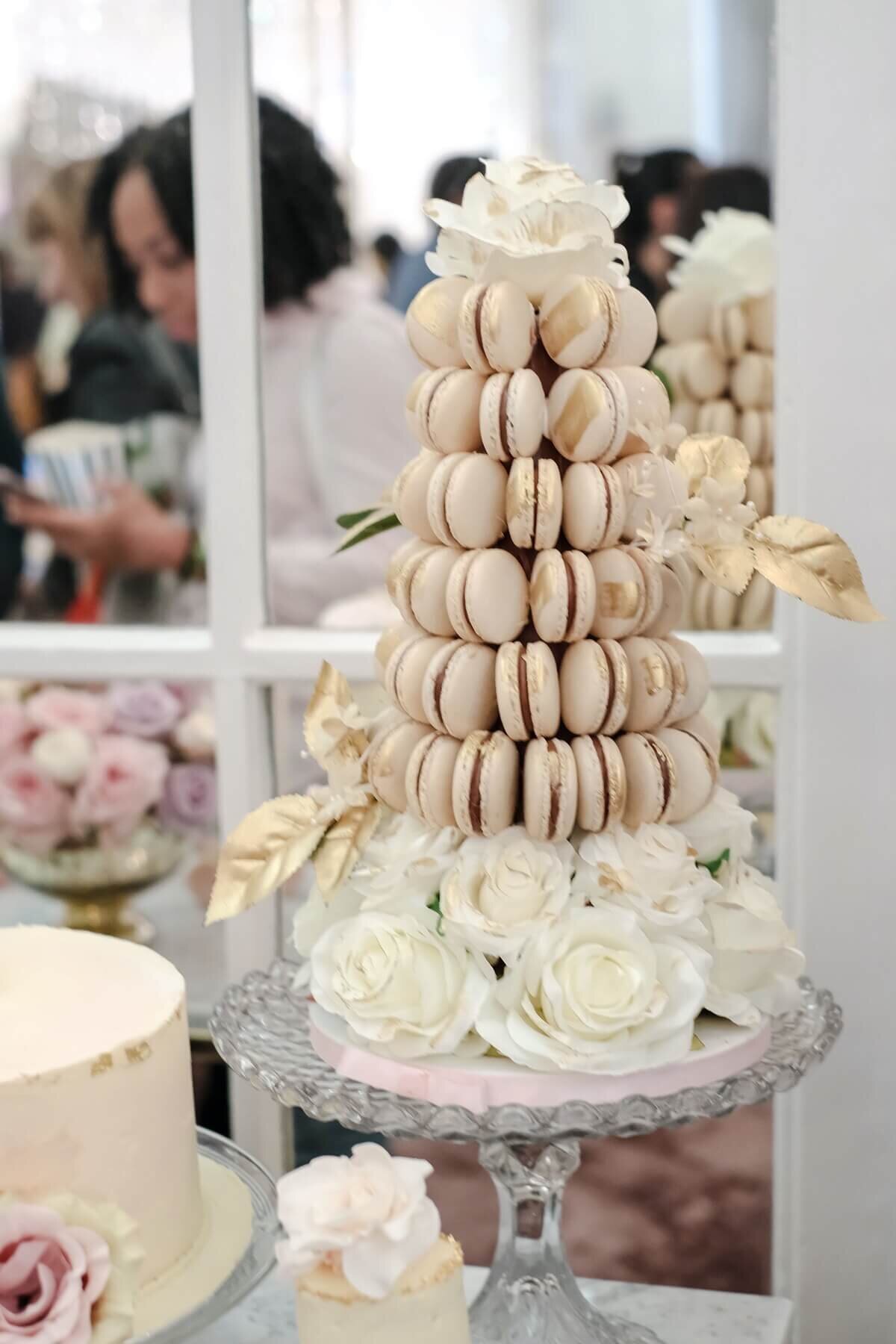 Gold macaroon tower sat on white roses on a glass cake stand