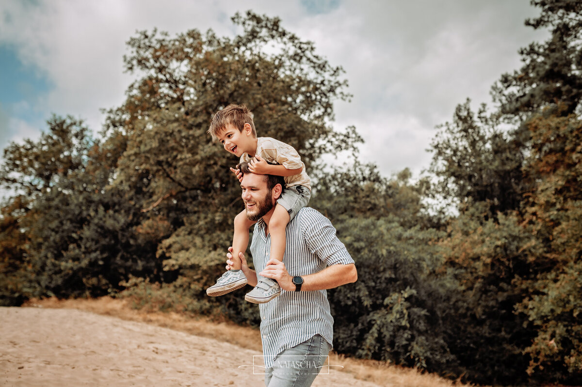 Zoon zit op de schouders van zijn vader en lopen langs het bos door de duinen bij de Bedafse Bergen in Uden