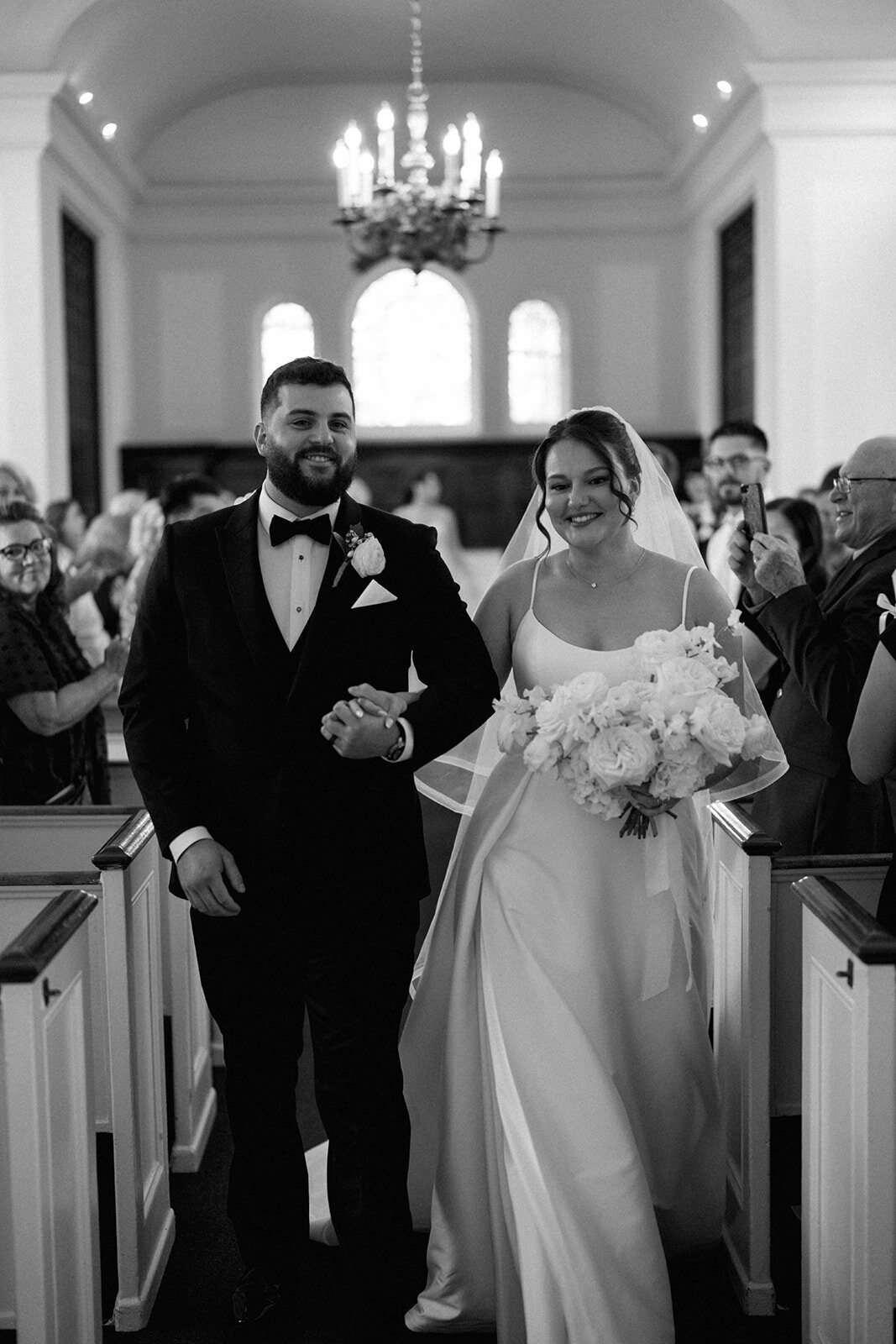 Bride and groom walking up the aisle inside Martha-Mary Chapel in Dearborn Michigan, classic church ceremony, joyful wedding recessional photo