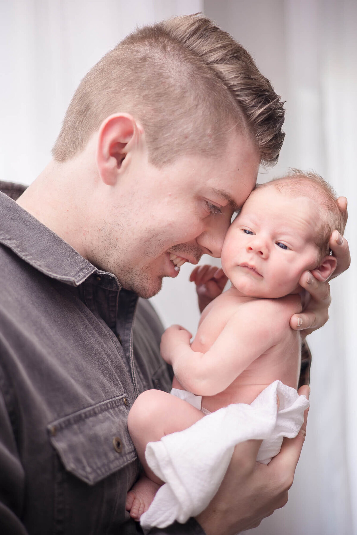 Dad lovingly looking at his newborn son and holding him up to his forehead