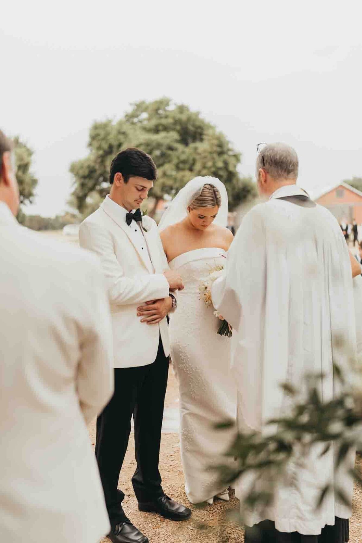 bride and groom bow their heads for prayer with pastor at the alter.